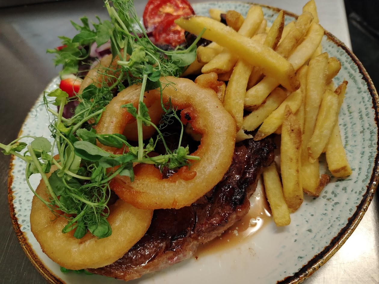 Rib eye steak with onion rings, chips and salad